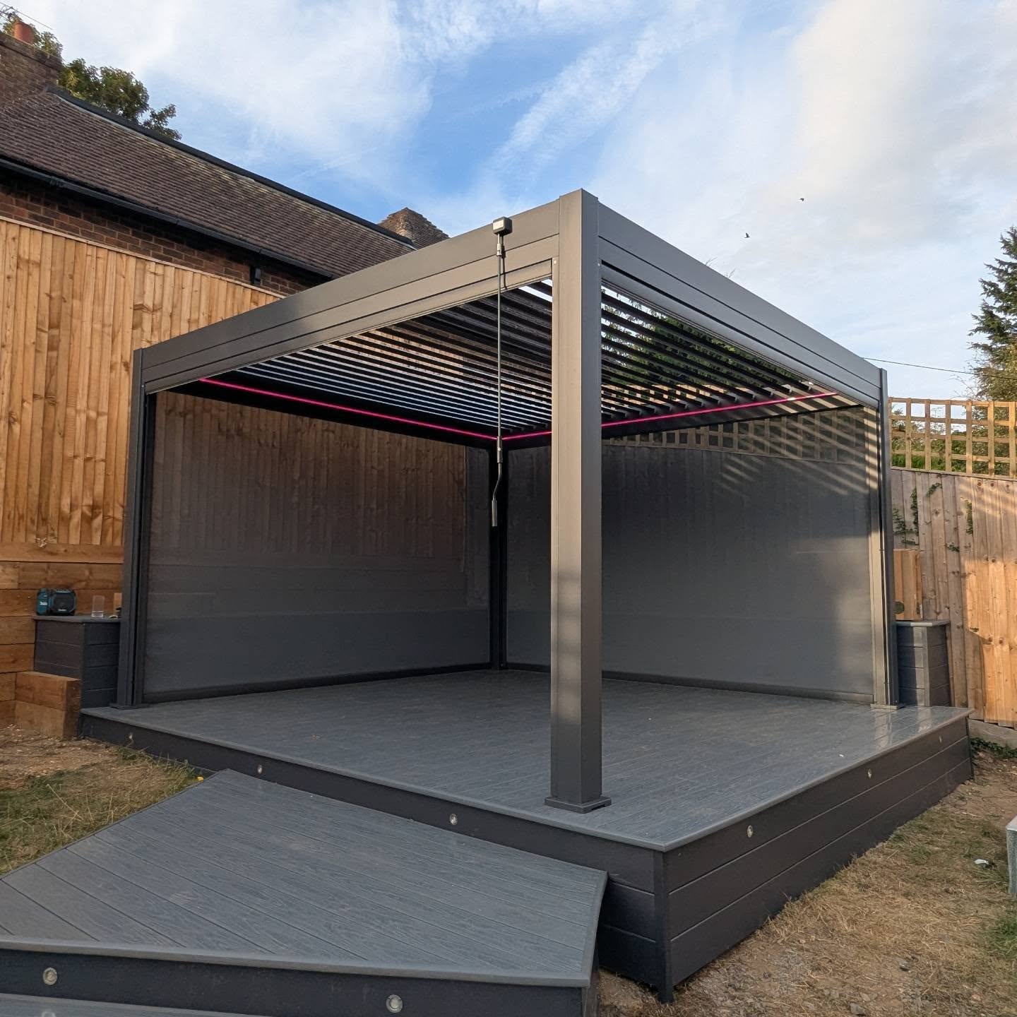 LuxShade™ 4×4m Aluminium Pergola with LEDs, Double-Layered Louvred Roof & 3 Blinds – shown in a garden setting